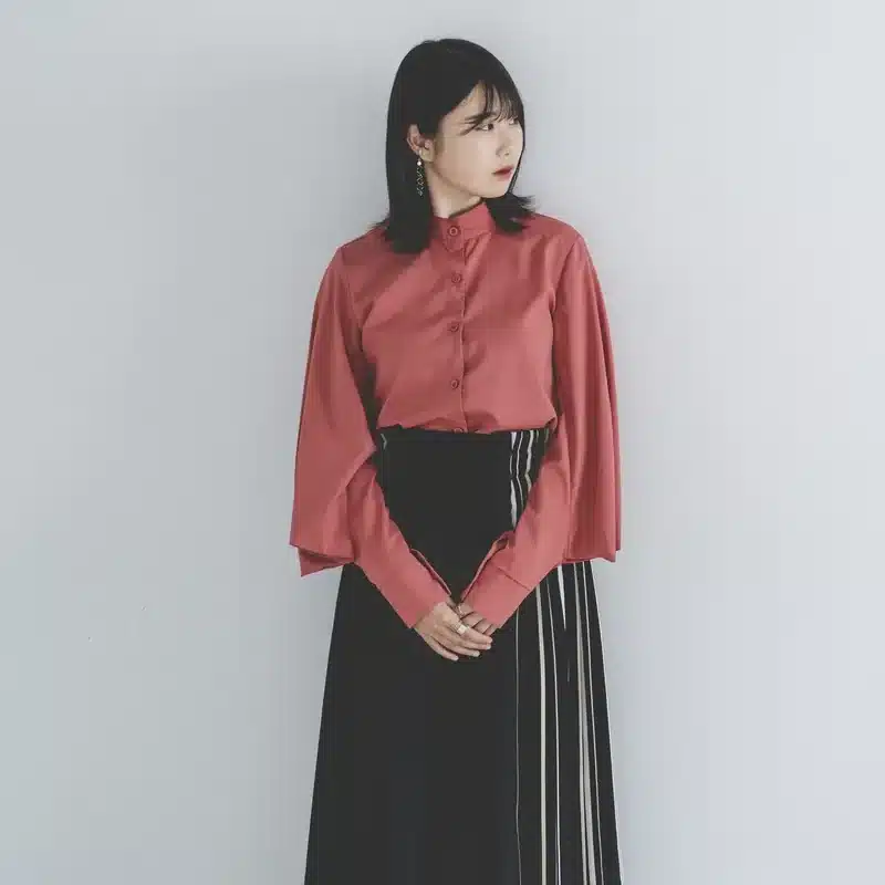 Nanobananaでポーズ変更を試す元になる、ピンクのブラウスを着て白い壁の前に立つ女性。